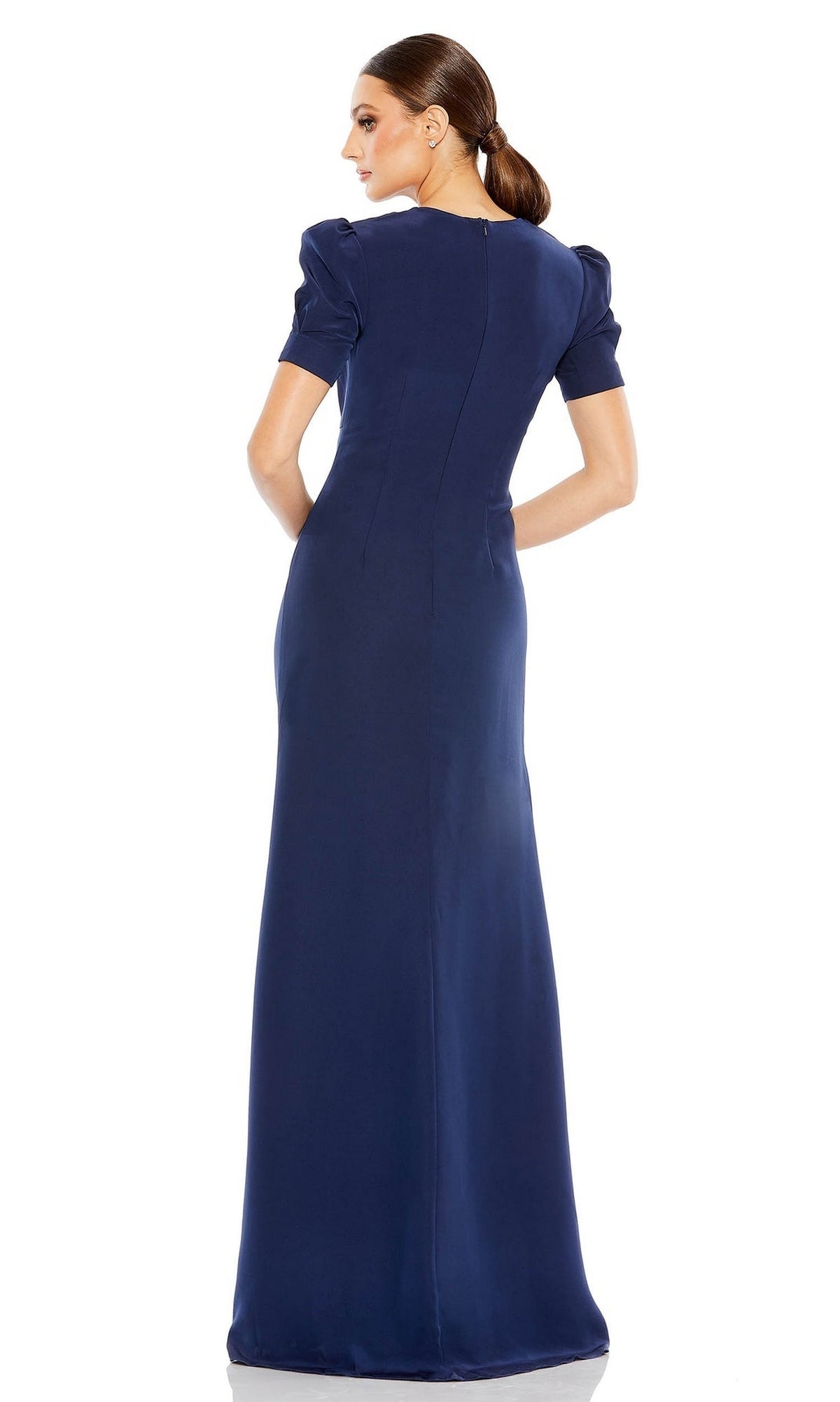 Woman stands with her back to the camera, wearing the Mac Duggal 2630 short-sleeve long formal dress in navy blue, her hair styled in a low ponytail.